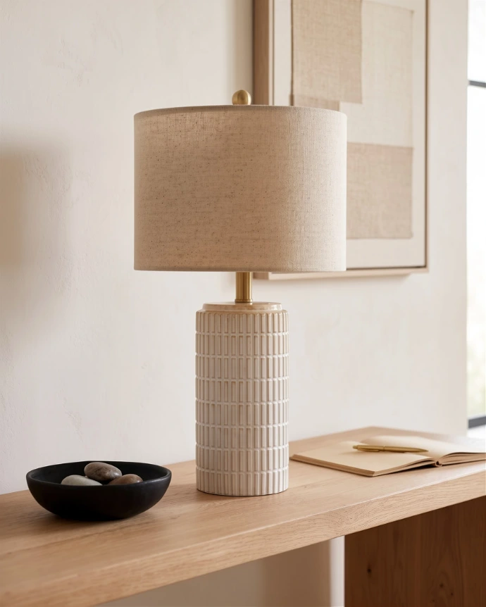 Minimalist white textured ceramic table lamp sitting on a wooden nightstand.